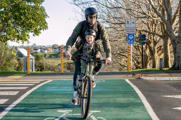 man riding a bike on a paved road, with a child on the top tube 