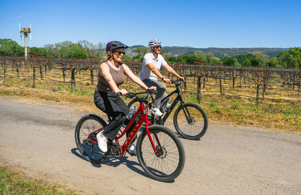 two people ride bikes through a vineyard