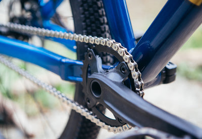 Close-up of a bicycle chain and sprocket with a blue frame.