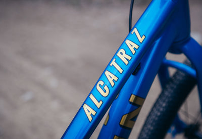 Blue bicycle frame with 'ALCATRAL' branding on a blurred background