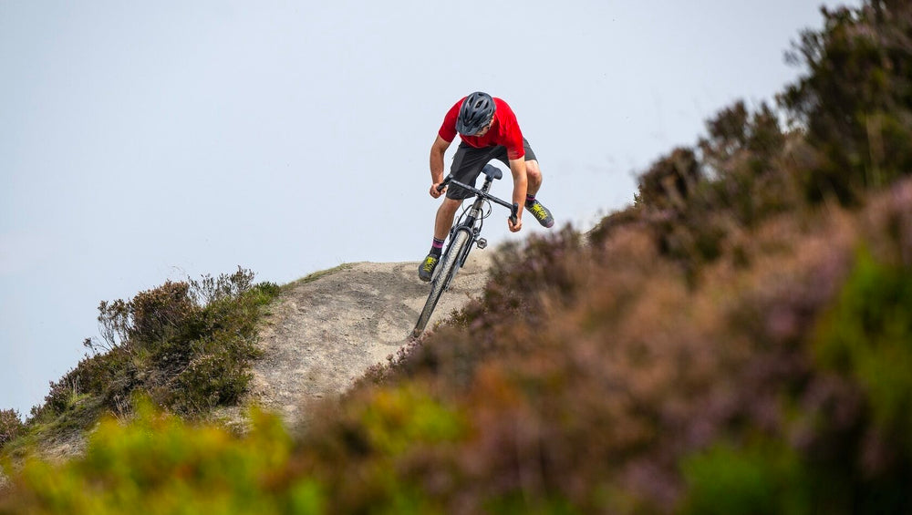 An image of a male cyclist riding a Marin Bikes Gestalt XR drop bar bicycle off-road through some heather