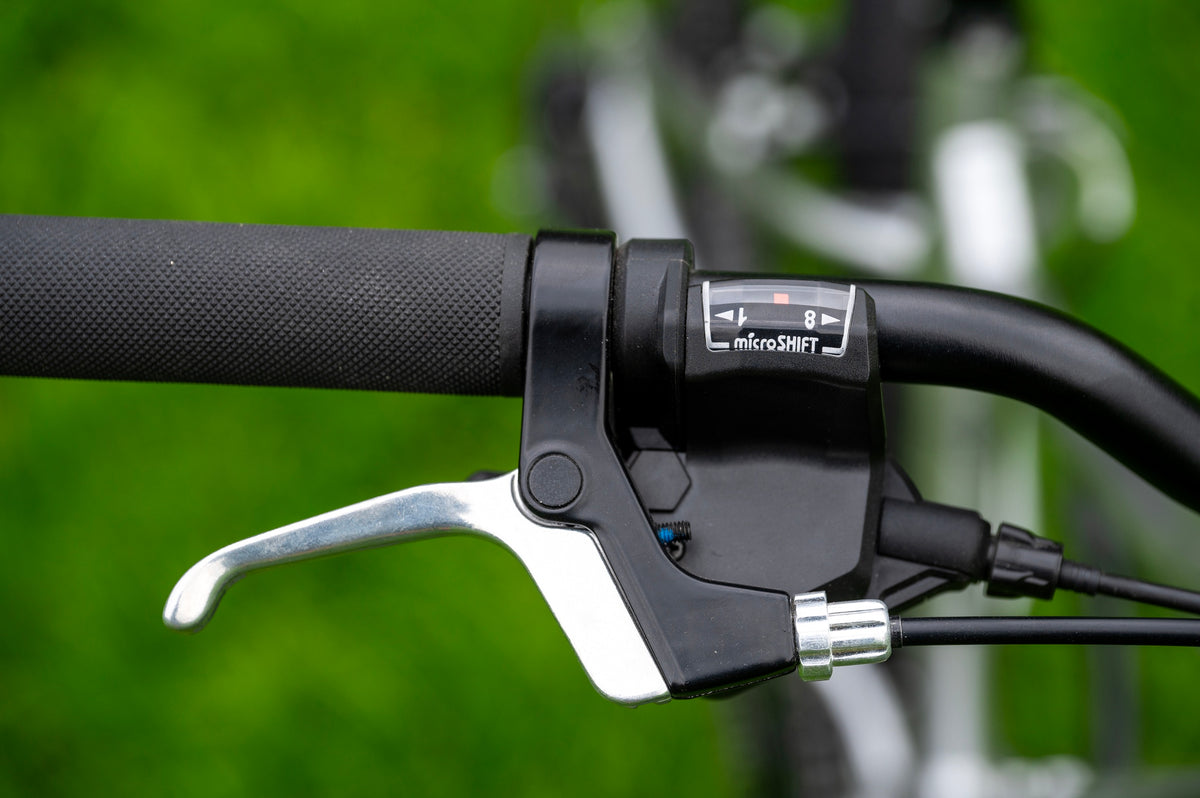 Close-up of a bicycle handlebar with a black brake lever and a small 'microSHIFT' label, set against a blurred green outdoor background.