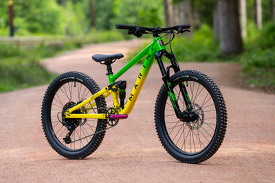 A Marin full-suspension mountain bike with a bright lime green and yellow frame, parked on a dirt path in a forest setting.