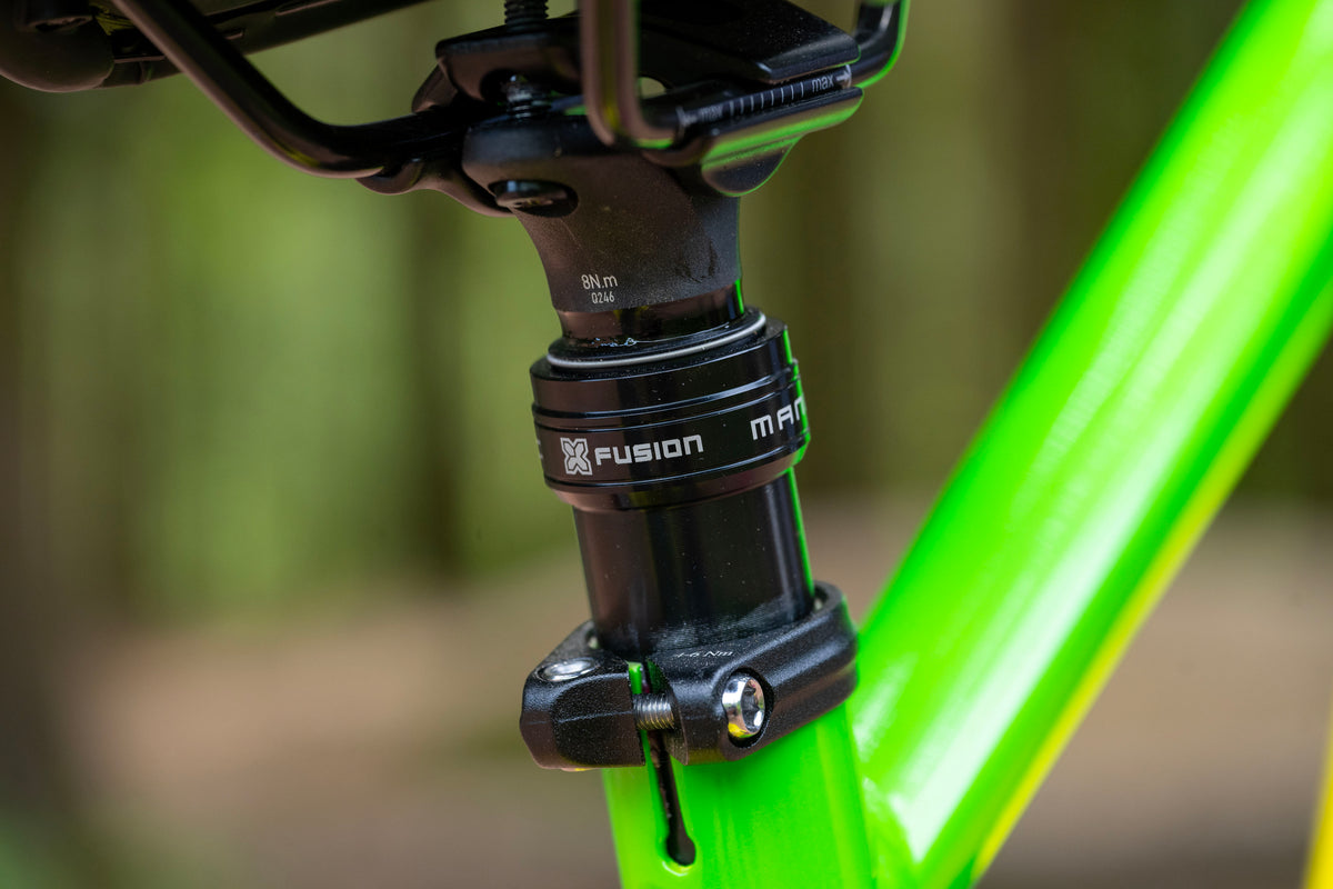 Close-up of a black M-Files Fusion bicycle headset mounted on a bright neon green frame, with a blurred outdoor background.