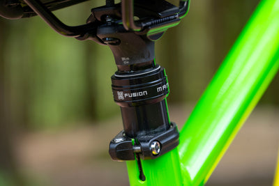 Close-up of a black M-Files Fusion bicycle headset mounted on a bright neon green frame, with a blurred outdoor background.
