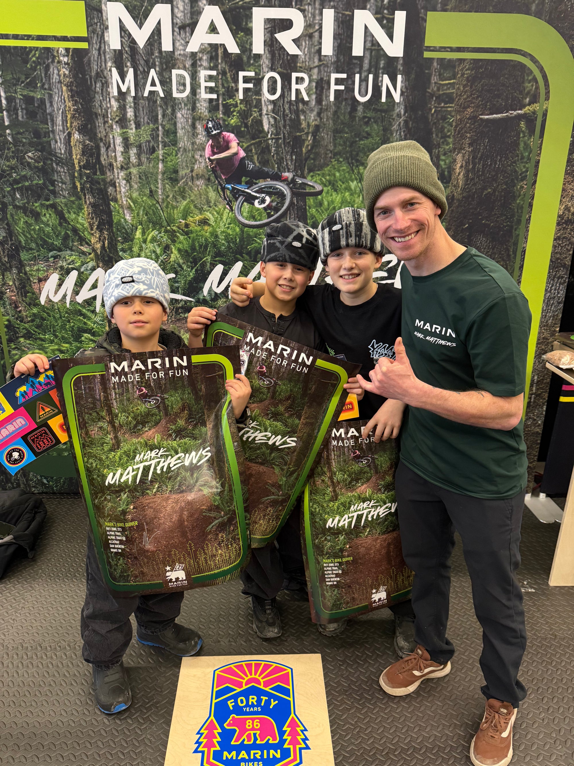 Four people holding Marin skateboard decks in front of a Marin bike poster.