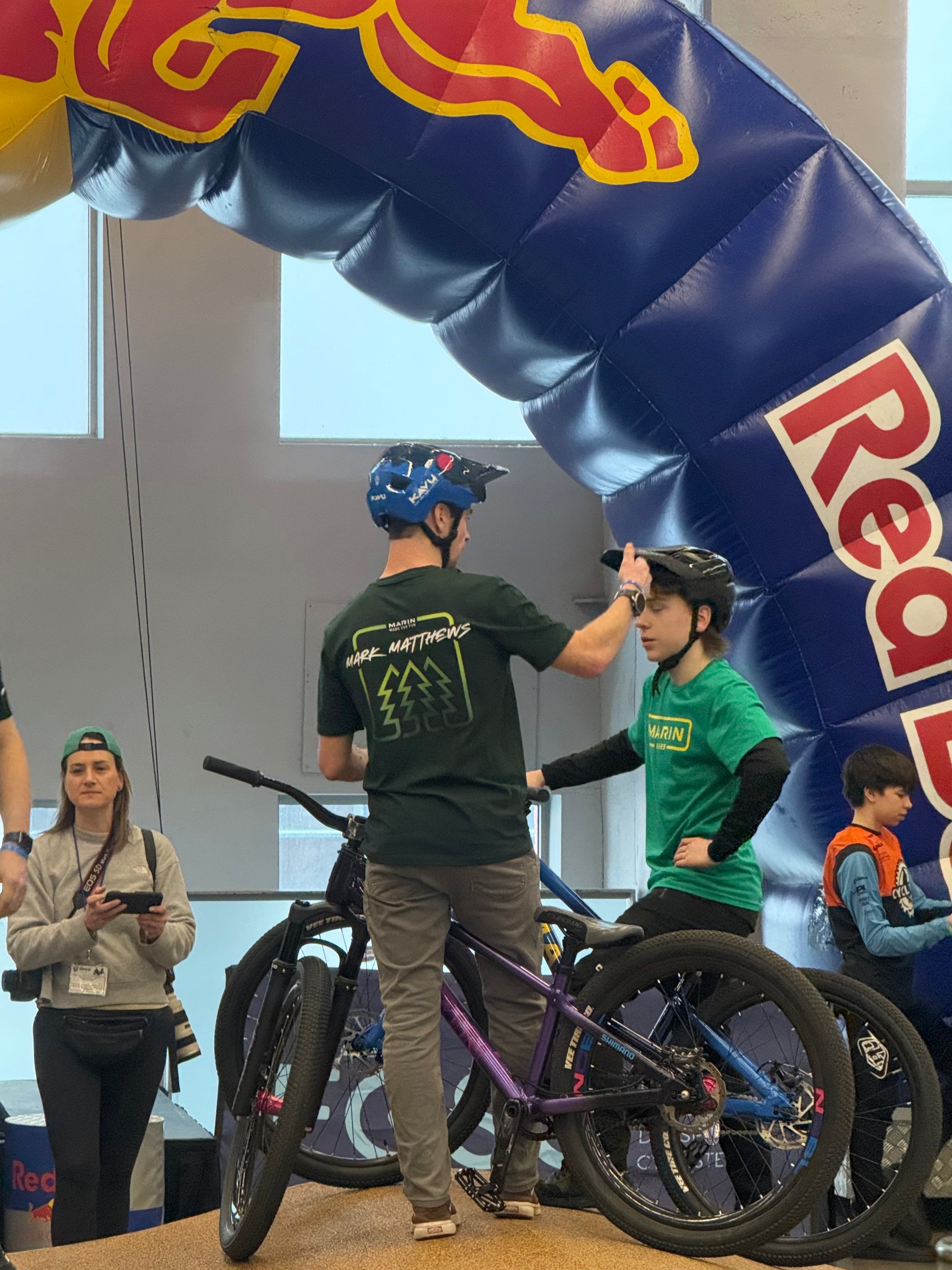 Two people with bicycles standing under a Red Bull inflatable archway.