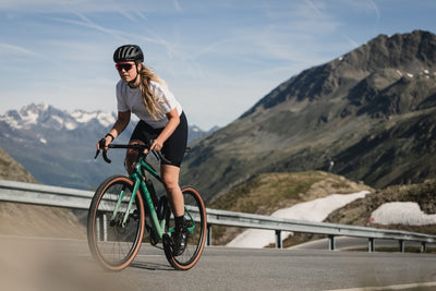 Person cycling on a mountain road with scenic mountains in the background