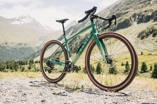 Green bicycle on a gravel path with mountains in the background
