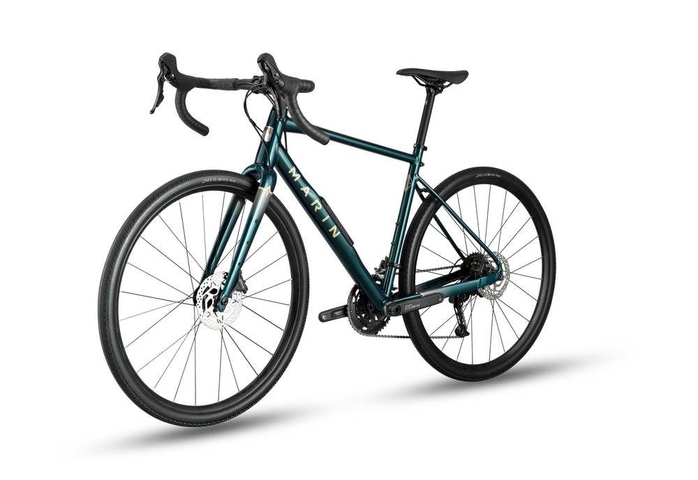 A dark teal mountain bike with black components, drop handlebars, and black wheels, shown from a three-quarters front angle on a white background with a soft shadow.