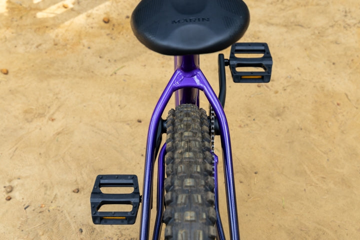 Purple bicycle frame with black seat and pedals on a sandy surface