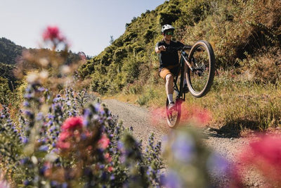 Man wheelies down a gravel track lined with flowers