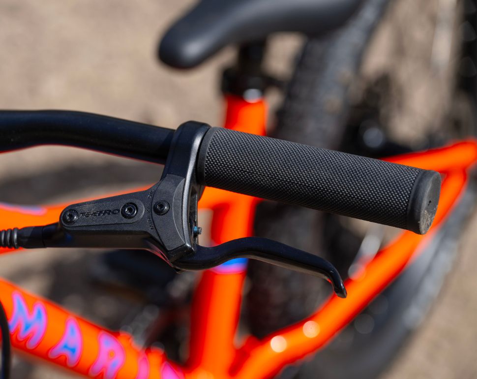 Close-up of a black SRAM brake lever mounted on a bright orange bicycle frame, with a textured black handlebar grip and blurred background.