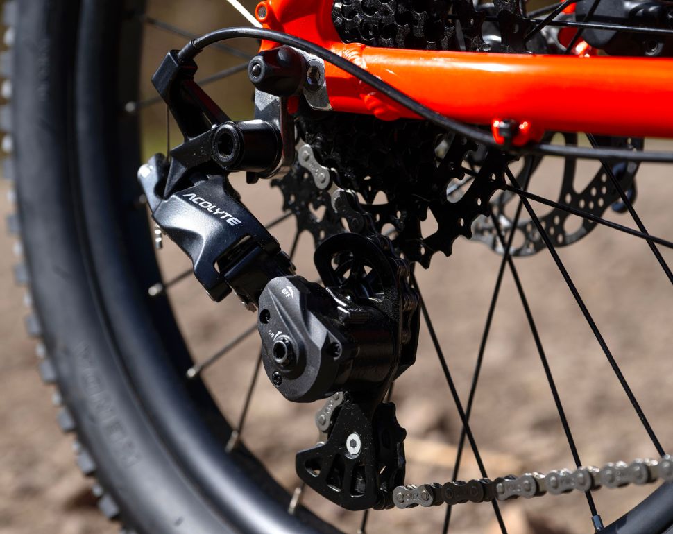 Close-up of a bicycle's rear derailleur system, showing black and silver components with an orange frame in the background.
