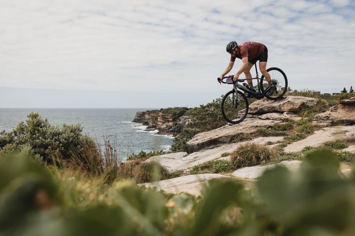 Person riding a bicycle on a rocky cliff overlooking the ocean