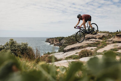 Person riding a bicycle on a rocky cliff overlooking the ocean
