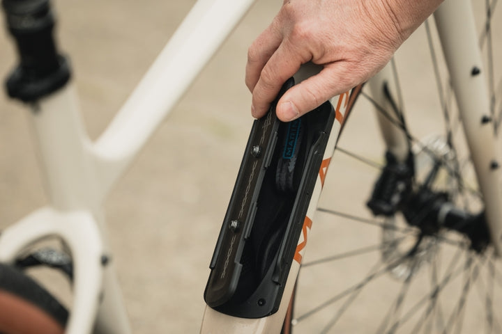 Person holding a black bike tool case with a bicycle in the background