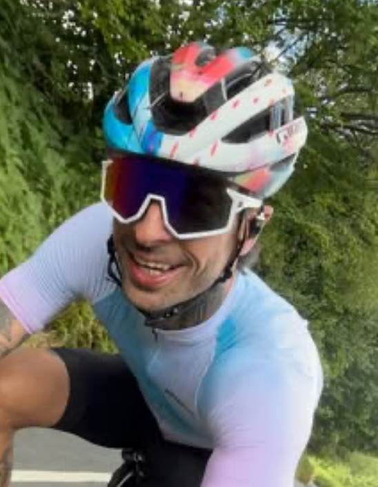 Cyclist wearing a colorful helmet and sunglasses with a green outdoor background