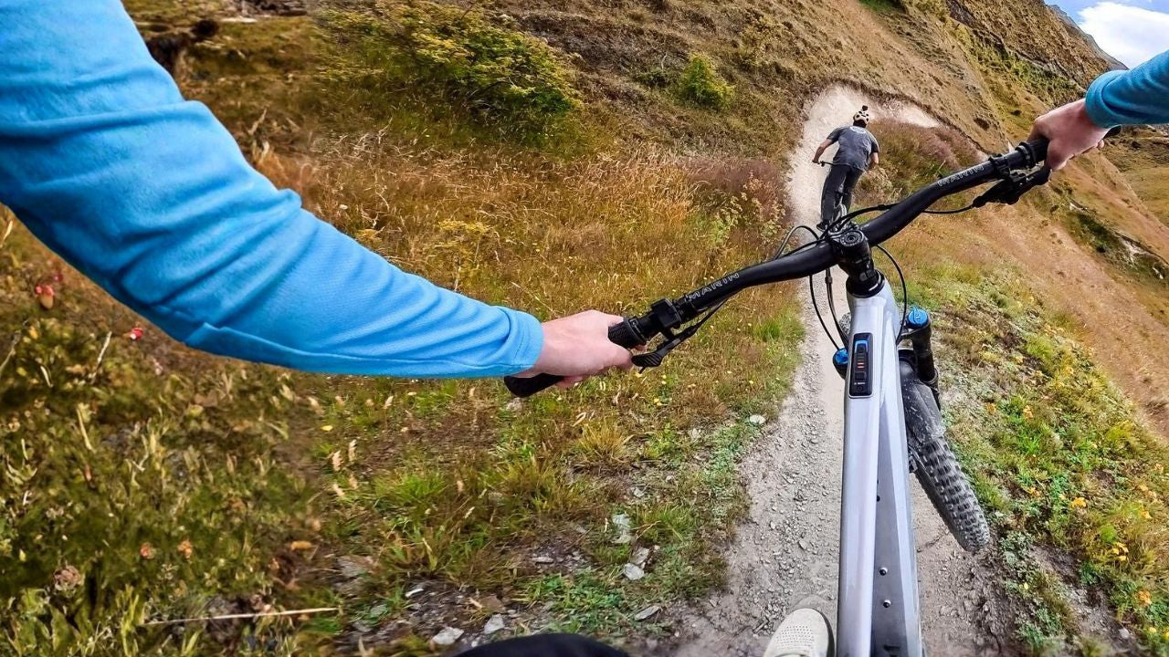 Two people on mountain bikes on a trail with a scenic background